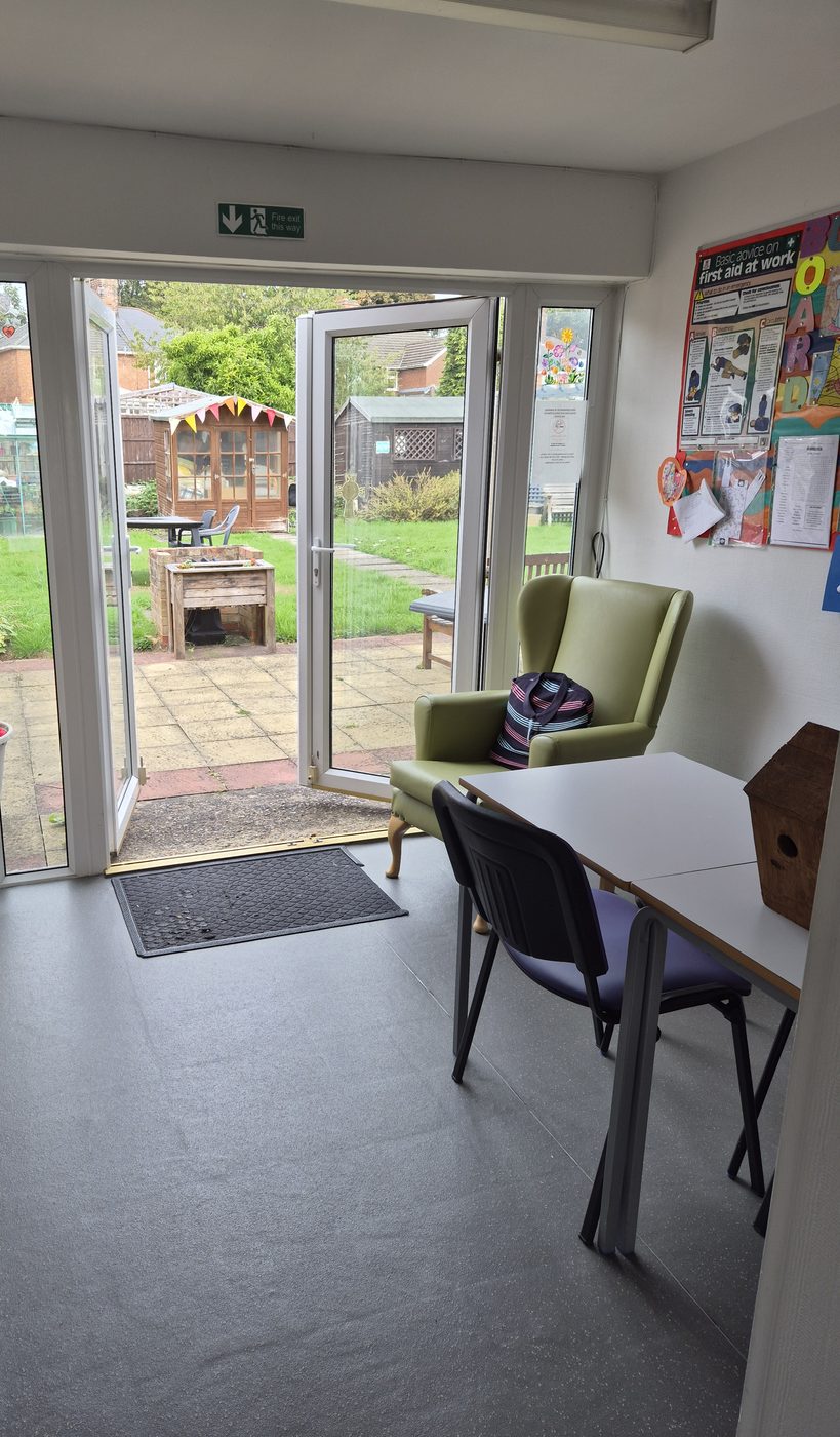 A light activity room with double doors open to a patio, garden and summer house.