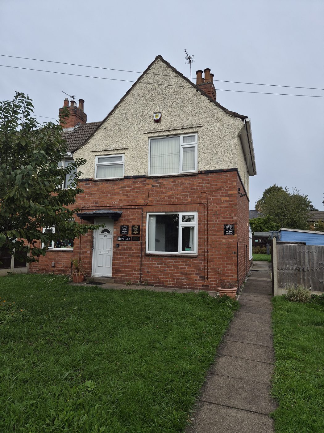 The front of Hope Lea, a red-brick house with a white front door and a small lawn.