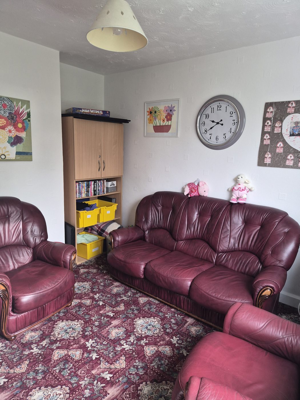 A cosy lounge with burgundy leather sofas, a bookcase of DVDs and games, and colourful artwork.